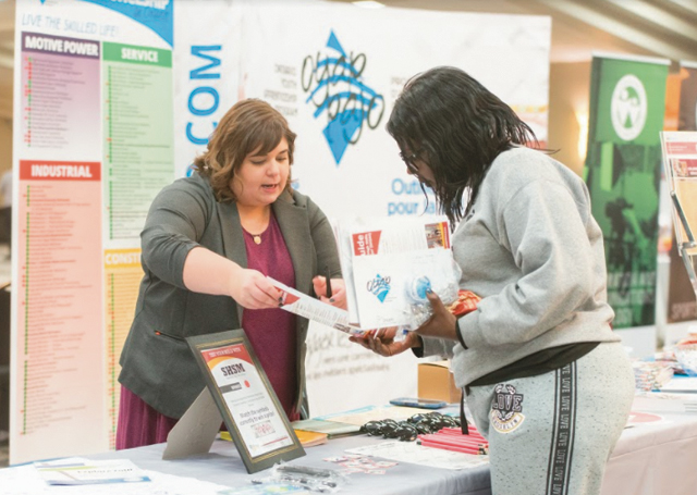 A OYAP teacher hands a student a pamphlet at a Build A Dreamcareer discovery expo in Kitchener, Ontario.